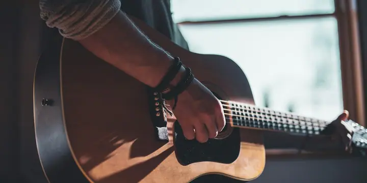 Hand schlägt die Saiten einer Akustikgitarre über dem Schallloch an